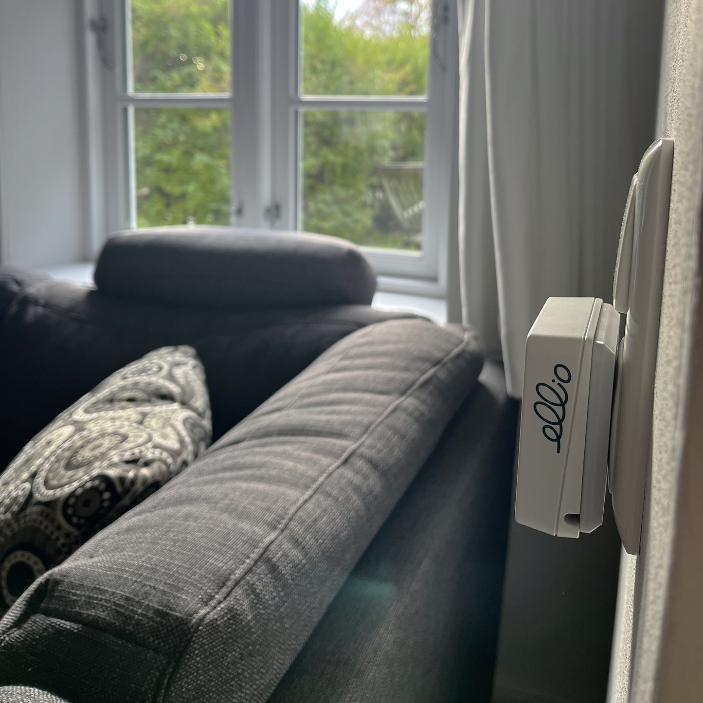 ellio Inaktivitätsmelder mit 230V Adapter an Steckdose befestigt im Wohnzimmern